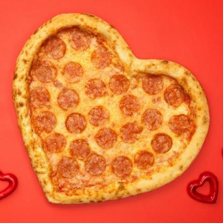 Pizza feferoni v obliki srca za valentinovo na ozadju rdečega papirja