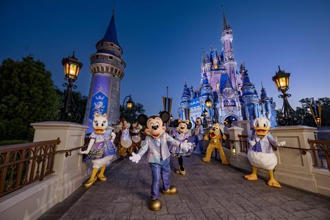 Mickey Mouse in prijatelji, oblečeni v svojo svetlečo se modo ob 50. obletnici, medtem ko pozirajo pred Pepelkinim gradom v parku čarobnega kraljestva